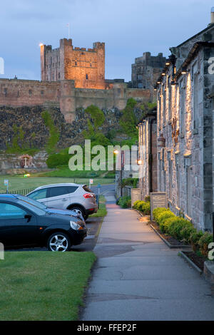 Bamburgh, Northumberland, England. Blick auf Fußweg zum beleuchteten Bergfried von Bamburgh Castle, Dämmerung. Stockfoto