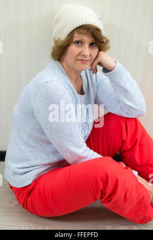 Erwachsene Frau in GAP und Pullover in der Nähe der Wand sitzen Stockfoto