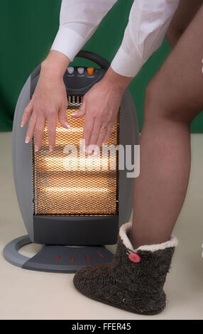 Frau, die Hände über elektrische Feuer wärmend Stockfoto