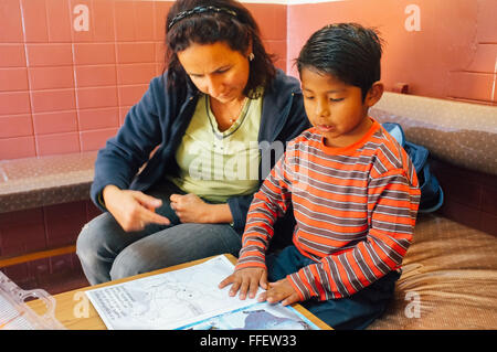 Reife kaukasischen Frau hilft ihr angenommenen Latin Boy mit seinen Hausaufgaben lesen Robin Hood während im Waisenhaus Stockfoto