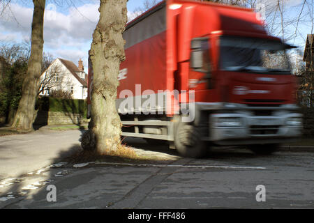 Ein Lastwagen fährt durch ein Baum wächst in der Mitte einer Kreuzung auf einer von Bäumen gesäumten Straße in einem grünen Vorort von Sheffield, Yorkshire UK Stockfoto