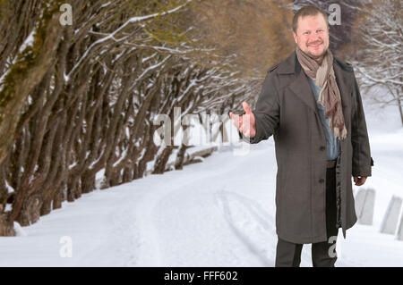 Mann mittleren Alters in einem Mantel und Schal suchen freundlich auf Winterpark Hintergrund Stockfoto