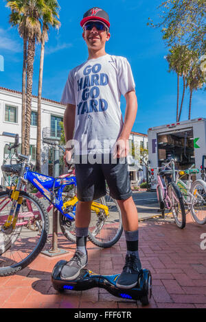 Ein männlicher Teenager hält und hält seinen Ritt auf seinem Hoverboard auf einem Bürgersteig in Santa Barbara, Kalifornien das Tragen von Sonnenbrillen. Stockfoto