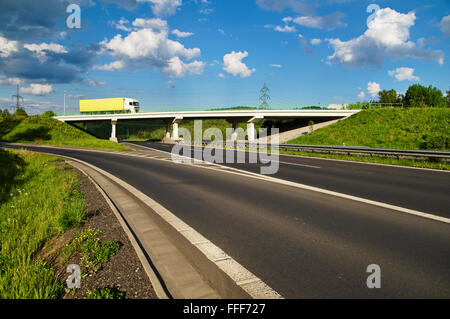 Brücke über eine leere Autobahn in der Landschaft, LKW, gehen über die Brücke, blauer Himmel mit weißen Wolken Stockfoto