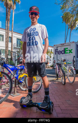 Ein männlicher Teenager hält und hält seinen Ritt auf seinem Hoverboard auf einem Bürgersteig in Santa Barbara, Kalifornien das Tragen von Sonnenbrillen. Stockfoto