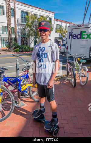 Ein männlicher Teenager hält und hält seinen Ritt auf seinem Hoverboard auf einem Bürgersteig in Santa Barbara, Kalifornien das Tragen von Sonnenbrillen. Stockfoto
