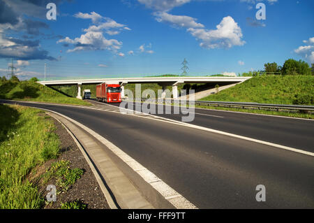 Brücke über eine leere Autobahn auf dem Lande, unter einer Brücke, vorbei an zwei Lastwagen, blauer Himmel mit weißen Wolken Stockfoto