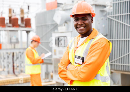 schöne afrikanische Techniker mit Kollegen auf Hintergrund im Umspannwerk Stockfoto