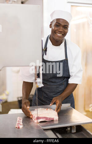 glückliche junge afrikanische männlichen Metzger Schneiden von Fleisch auf Bandsäge Stockfoto
