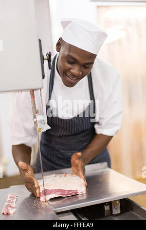 gut aussehende afroamerikanische Metzger schneiden Fleisch auf Bandsäge Stockfoto