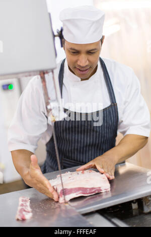 gut aussehend Metzger schneiden Fleisch auf Bandsäge Stockfoto