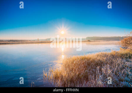 Sonnenaufgang über den Fluss. Herbst Frost gefrorenen Fluss mit dünnem Eis bedeckt. Grass bedeckt mit Frost. Sonnenaufgang, Sonnenuntergang über Herbst Stockfoto