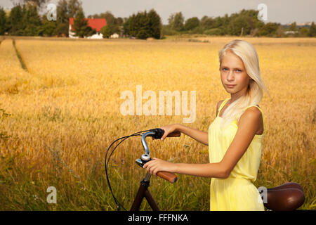 Junges Mädchen mit einem Fahrrad auf dem Weizen Feld Hintergrund. Stockfoto