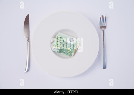 stilvolles Design in weißes Runde Suppenteller mit Wad Euro Bargeld Geld 100 Banknote zwischen Silber Gabel und Messer auf weiß ta Stockfoto