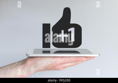Soziales Netzwerk-Daumen hoch Symbol mit dem Pluszeichen. Konzept des mobile computing und social Media. Hand mit Tablet oder Smartphone. Stockfoto