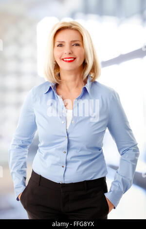 Taille bis Porträt des mittleren Alters Geschäftsfrau. Reife Frau im Büro stehen und blickte in die Kamera Lächeln. Stockfoto