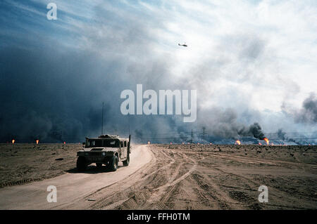 Ein M998 High Mobility Multipurpose Wheeled Fahrzeug (HMMWV) fährt entlang einer Straße in der kuwaitischen Wüste nach Operation Desert Storm.  Im Hintergrund brennen Ölquellen in Brand gesetzt, durch die sich zurückziehende irakische Truppen. Stockfoto