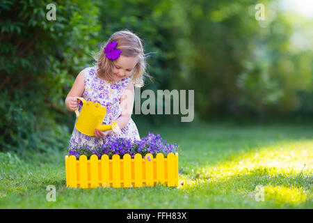 Kind im Garten arbeiten. Kinder im Garten. Kinder, die Blumen gießen. Kleines Mädchen mit Wasser kann auf einem grünen Rasen Stockfoto