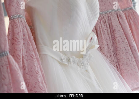 Eine traditionelle weiße Hochzeit Kleid hing unter vier rosa Brautjungfern Kleider Stockfoto