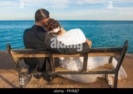 Braut und Bräutigam Paar sitzt auf einer Holzbank mit Blick auf tropische Meer Stockfoto