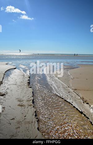 Süßwasser-Datenstrom in ein funkelndes Meer bei Camber Sands in Sussex, England, mit Kite Surfers aus auf See Stockfoto