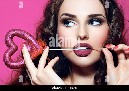 Gesicht des Mädchens. Fest. Herz in den Händen. Rosa Make-up. Glamour. Stockfoto