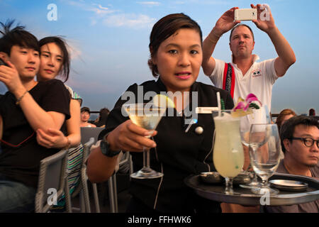 Kellnerin mit Cocktails in der Hand. Banyan Tree auf dem Dach Vertigo & Moon Bar, Restaurant, Bangkok, Thailand. Blick auf die Stadt, Stockfoto