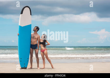 Glückliches junges Paar stehend mit einem Surfbrett am Strand. Stock Bild. Stockfoto