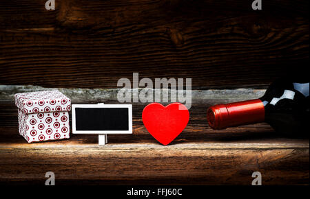 Rotes Herz aus Holz, Flasche Wein, Geschenk-Box und kleinen Tafel auf Holzbrett. Liebe-Konzept im Vintage. Valentines Day. Stockfoto