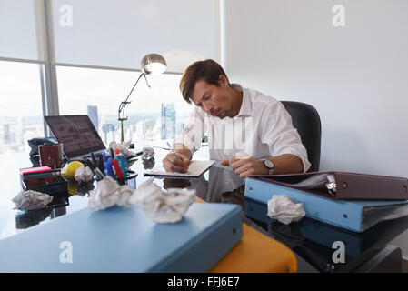 Corporate Manager in modernen Büro versucht, eine Arbeit zu schreiben. Der Mann ist frustriert und hält am Schreibtisch Papier anschrauben Stockfoto