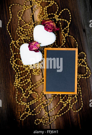 Zwei weiße Herz geformten Kekse, Blackboard, goldenen Perlen und getrockneten Rosen auf sehr alten Holzbrett. Happy Valentines Day. Lebenshaltungen Stockfoto