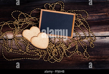 Zwei herzförmige Kekse, Blackboard und goldene Perlen auf sehr alten Holzbrett. Happy Valentines Day. Romantische Komposition. Stockfoto