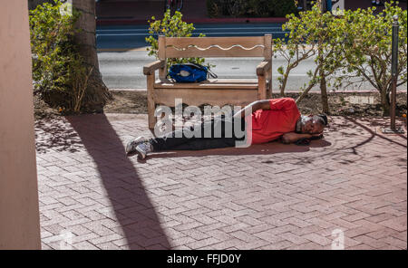 Ein Mann mittleren Alters afro-amerikanischen Obdachloser schläft ausgestreckt, auf dem Bürgersteig auf der State Street in Santa Barbara, Kalifornien. Stockfoto