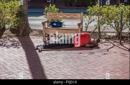 Ein Mann mittleren Alters afro-amerikanischen Obdachloser schläft ausgestreckt, auf dem Bürgersteig auf der State Street in Santa Barbara, Kalifornien. Stockfoto