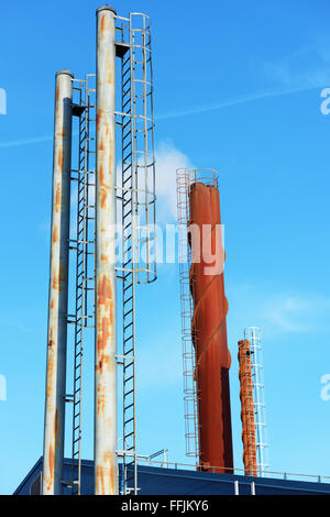 Es gibt viele verschiedene Schornsteine vor blauem Himmel. Etwas Rauch kommt aus einer von ihnen. Stockfoto