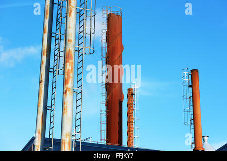 Es gibt viele verschiedene Schornsteine vor blauem Himmel. Etwas Rauch kommt aus einer von ihnen. Stockfoto