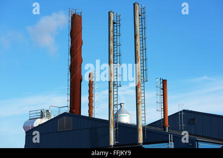 Es gibt viele verschiedene Schornsteine vor blauem Himmel. Etwas Rauch kommt aus einer von ihnen. Stockfoto