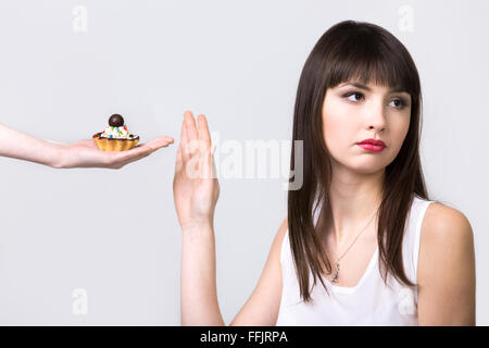 Junge resolute Diät schöne Frau weigert Torte Kuchen mit Sahne und Schokolade, Studio, gesunden Lifestyle-Konzept, graue Rückseite Stockfoto