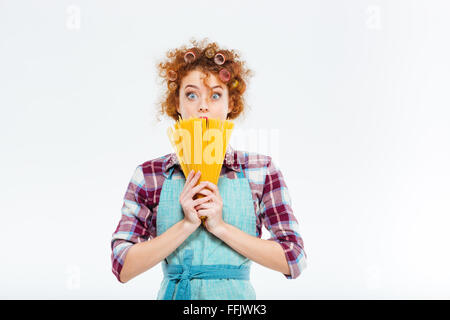 Überrascht niedlich schöne junge Hausfrau in Küchenschürze versteckt sich hinter ungekocht Spagetti auf weißem Hintergrund Stockfoto