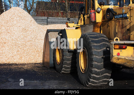 Brakne-Hoby, Schweden-7. Februar 2016: Eine gelbe Volvo BM Frontlader mit Schaufel nach unten laden Biokraftstoff aus einem Haufen von Hackschnitzel Stockfoto