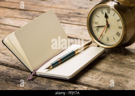 Geöffneten Notizbuch mit Füllfederhalter und Wecker auf Schreibtisch aus Holz. Tagebuch-Planung-Hintergrund Stockfoto