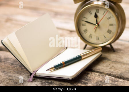 Geöffneten Notizbuch mit Füllfederhalter und Wecker auf Schreibtisch aus Holz. Tagebuch-Planung-Hintergrund Stockfoto