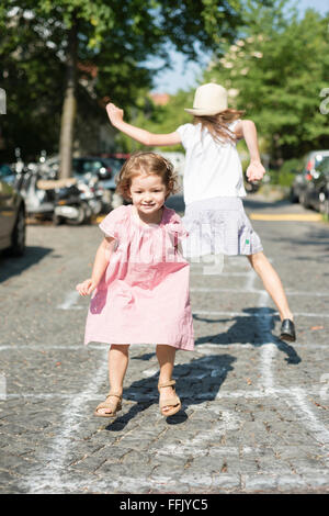 Zwei Mädchen spielen Himmel und Hölle auf Kopfsteinpflaster Stockfoto