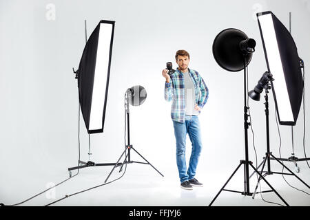 Voller Länge Porträt eines jungen Fotografen stehend mit Foto-Kamera im studio Stockfoto