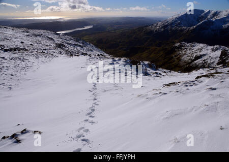 Fußspuren im Schnee über dem Kupfer-Minen-Tal von den Hängen des Wetherlam mit Coniston Greis auf die Skyline Stockfoto