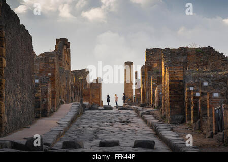 Pompeji Tourismus, Blick bei Sonnenuntergang von drei Besuchern der antiken Stadt Pompeji stehend in der Via dell' Abbondanza, Italien Stockfoto