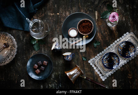 Zutaten für türkischen Kaffee (Kaffee, Zucker, Wasser), Kaffeetassen und traditionellen Kaffeekanne sind auf eine Altholz angezeigt. Stockfoto