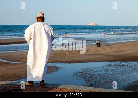 Ein omanischer Mann In traditioneller Kleidung blickt über den Strand von Muscat, Sultanat von Oman Stockfoto