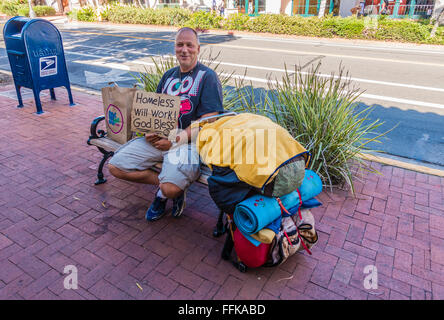 Ein im mittleren Alter männlicher Bettler auf einer öffentlichen Bank auf einen State Street Bürgersteig mit einem Schild, das sagt "Obdachlose, funktioniert, Gott segne" Stockfoto