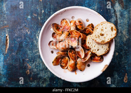 Vongole Muscheln mit Petersilie und Tomatensauce in Vintage Keramik Sieb auf blauem Hintergrund Stockfoto